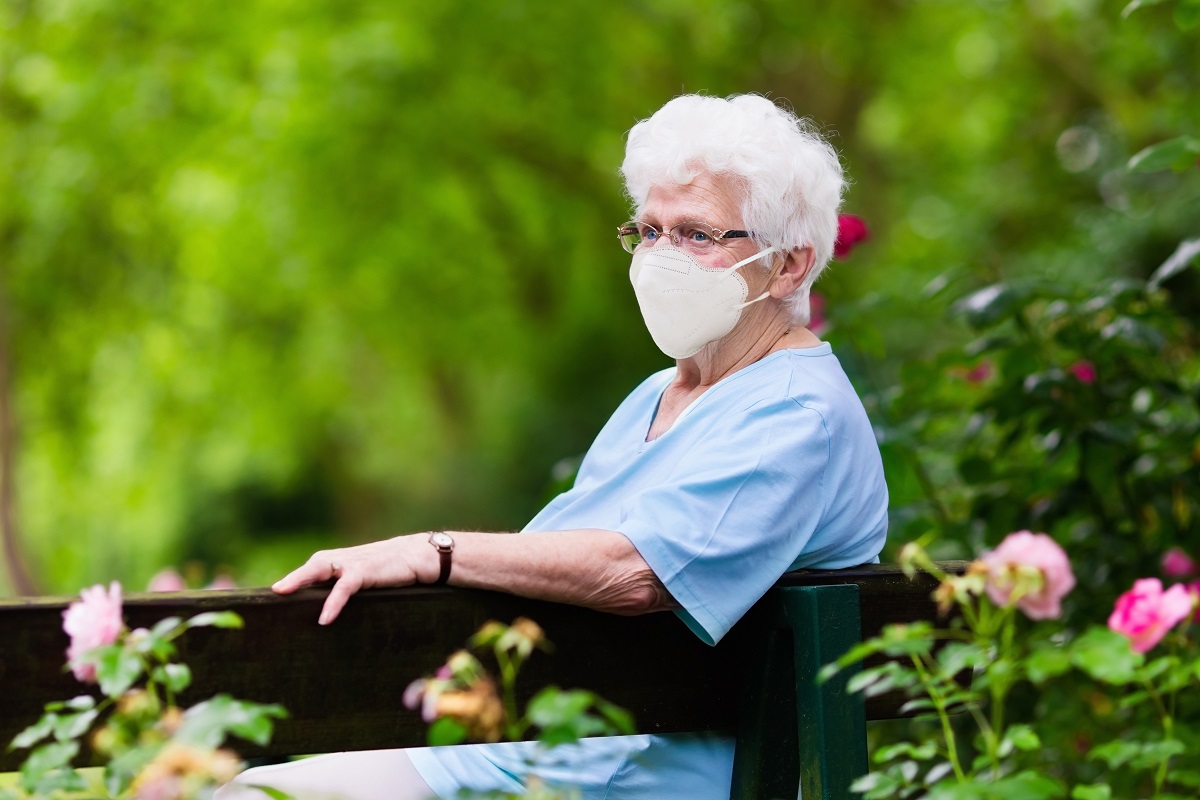 senior with face mask sitting on a bench at senior living community