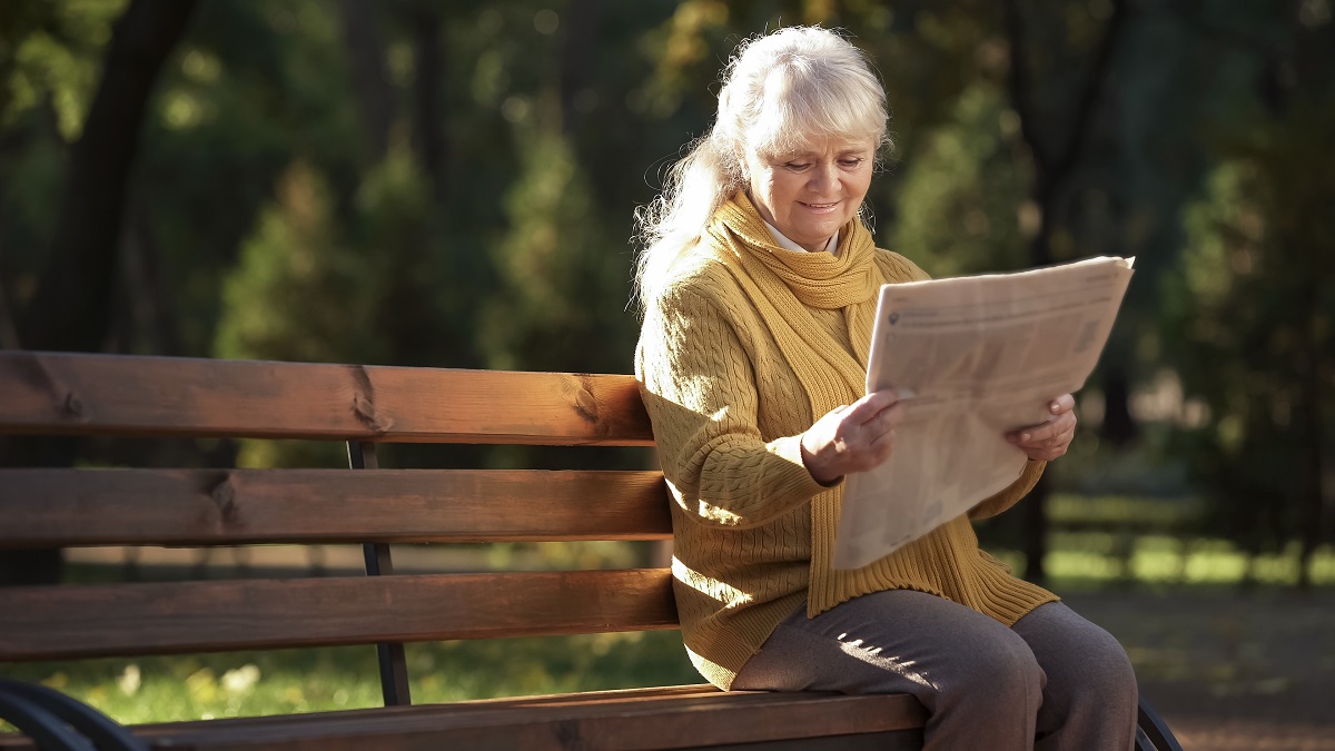Senior woman reading the paper at a park bench