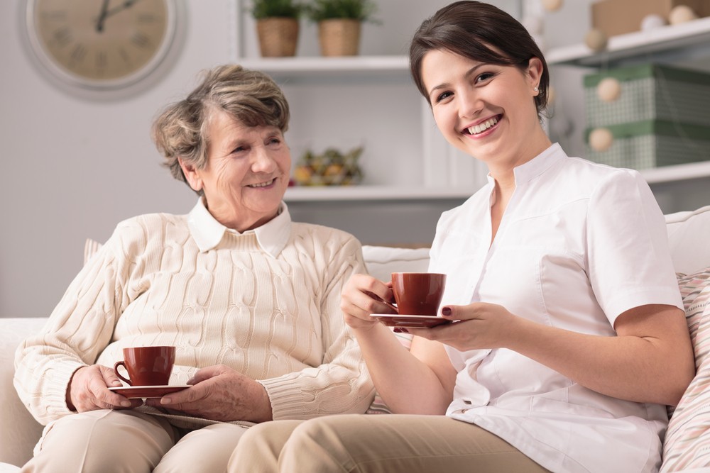 Senior woman drinking tea or coffee with caregiver