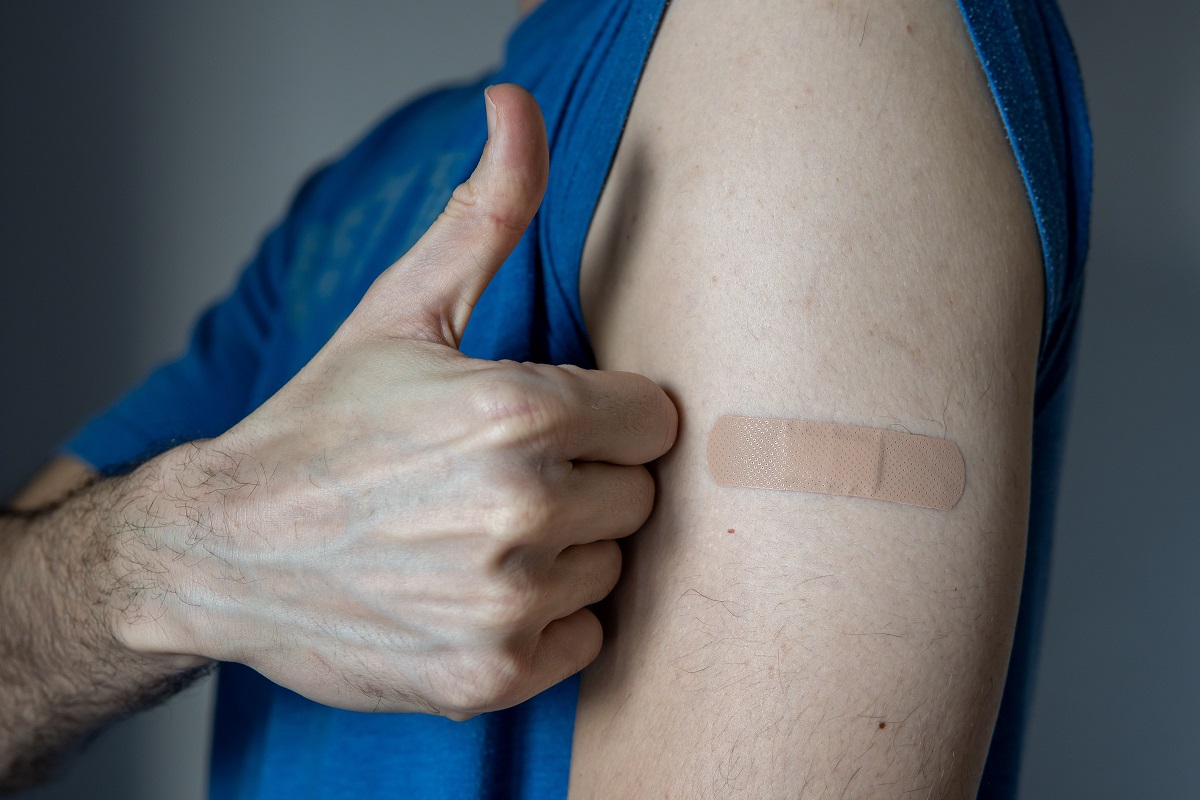 A man's arm with an adhesive bandage after injection of vaccine or a scratch on the skin. Satisfied and showing thumbs up or like. First aid medical and healthcare concept. After vaccination treatment