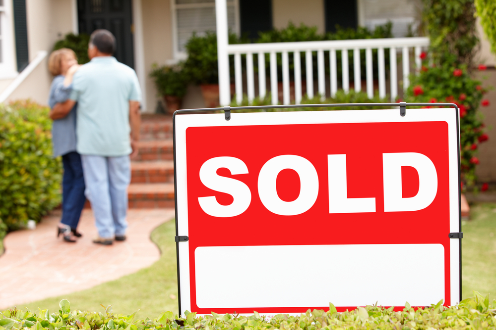 A sold sign in front of a house and a senior couple happy to have sold their home