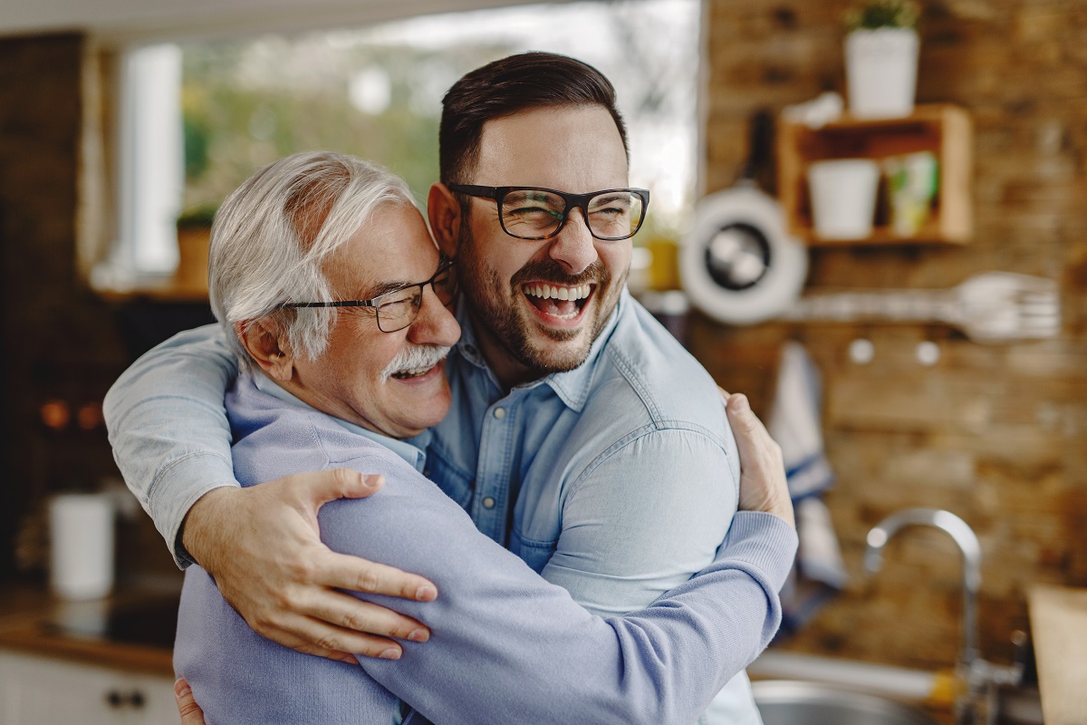 Cheerful man and his senior father embracing while greeting in the kitchen