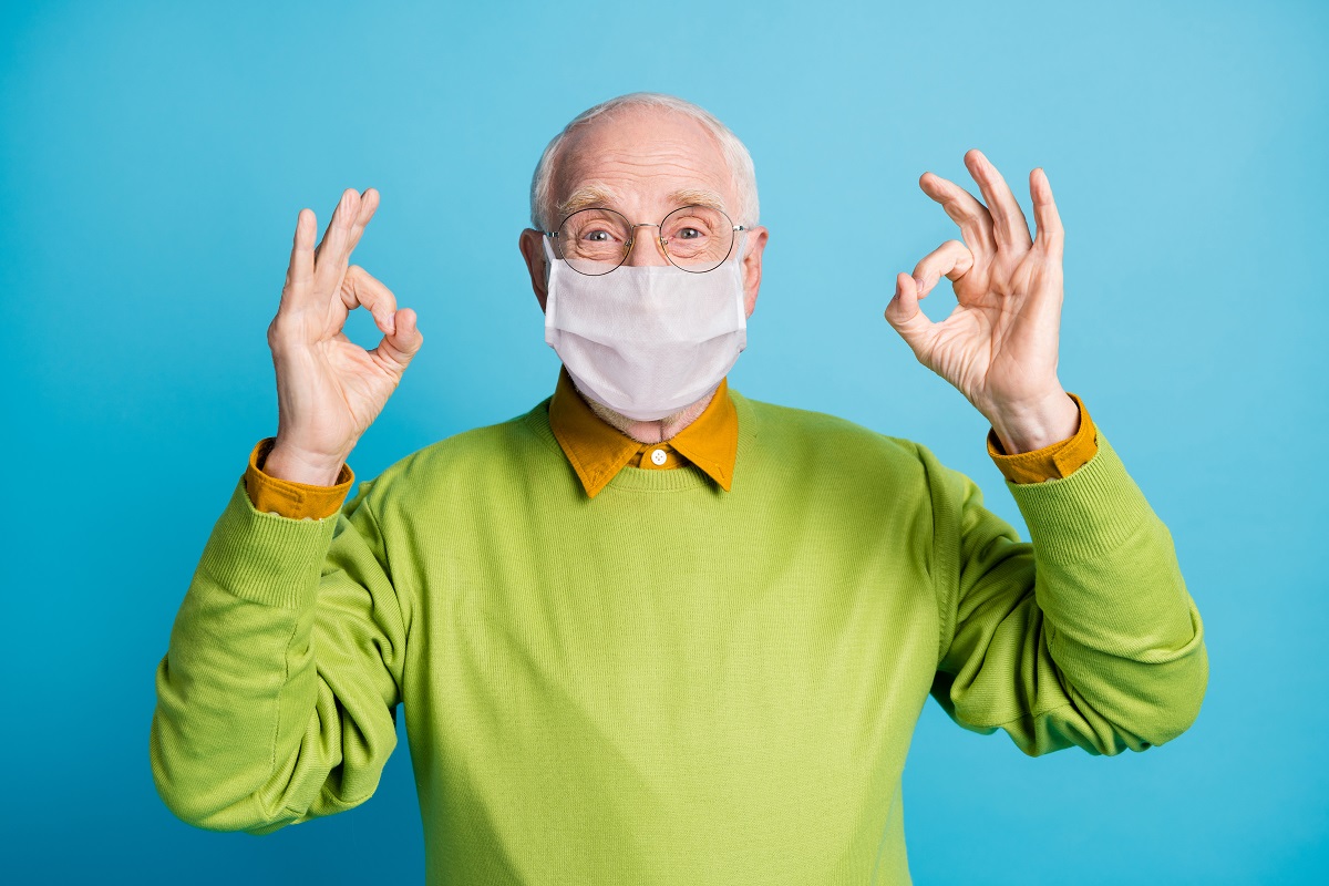 senior raising two arms with an okay symbol wearing a white face mask